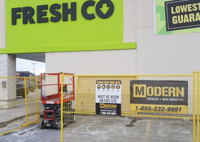 Yellow temporary fencing set up in front of a Fresh Co supermarket with a Modern Fence Rental sign on it.